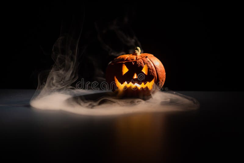 Halloween, orange pumpkin with a scary luminous face on a dark background. Gray thick smoke comes out. royalty free stock photos Halloween, orange pumpkin with a scary luminous face on a dark background. Gray thick smoke comes out. royalty free stock photos