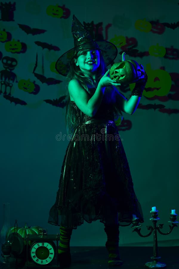 Halloween party and decorations concept. Girl with happy face. On dark green background with bats and pumpkins decor. Little witch wearing black hat. Kid in royalty free stock photography Halloween party and decorations concept. Girl with happy face. On dark green background with bats and pumpkins decor. Little witch wearing black hat. Kid in royalty free stock photography