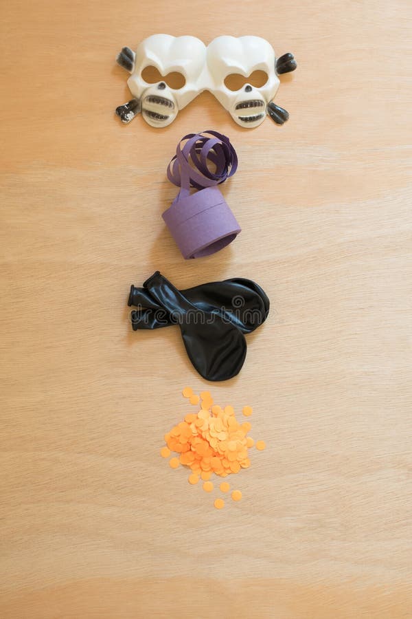 Halloween party elements. Plastic skull glasses, purple streamer, black balloons and orange confetti on a wooden surface.