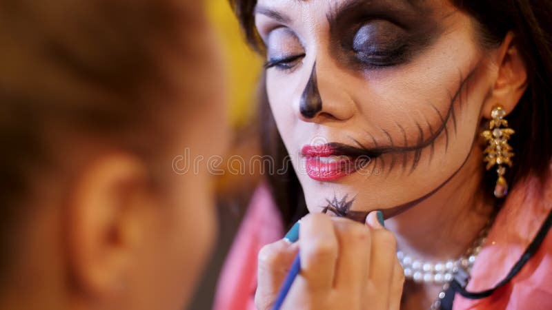 Halloween party, make-up artist draws a terrible makeup on the face of a brunette woman for a Halloween party. in the