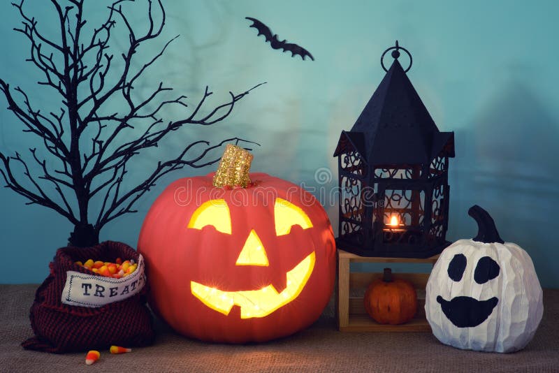 Halloween still life scene with carved pumpkin, lantern, treats bag, and ghost gourd with teal background with night shadows. It stock images