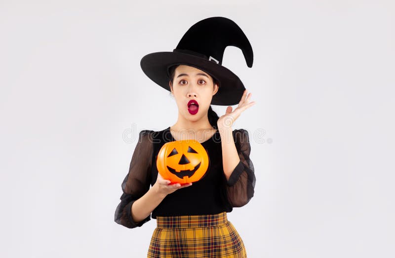 Halloween theme, young pretty asian woman in black halloween costume wearing witch hat holding orange pumpkin bucket posing surprised , excited and wow on white background. Halloween theme, young pretty asian woman in black halloween costume wearing witch hat holding orange pumpkin bucket posing surprised , excited and wow on white background.