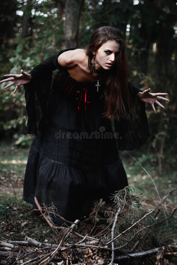 Halloween Witch in a dark forest. Beautiful young woman in witches costume . Halloween art design. Horror Background For Halloween