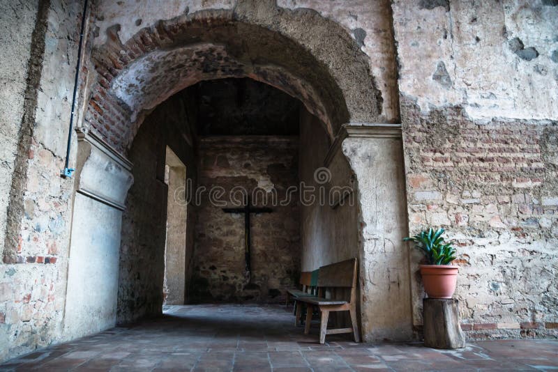 Hallway of Hermano Pedro monestery with cross, plant and arch, Antigua, Guatemala