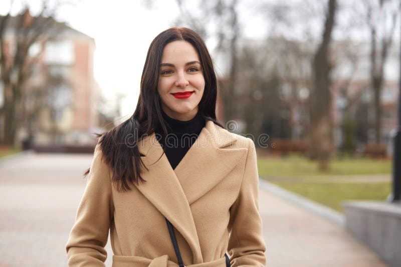 Halvt längdskott av den attraktiva unga kvinnan i elegant beige lag som går på gatan Den förtjusande brunettkvinnan spenderar hen royaltyfri bild Halvt längdskott av den attraktiva unga kvinnan i elegant beige lag som går på gatan Den förtjusande brunettkvinnan spenderar hen royaltyfri bild