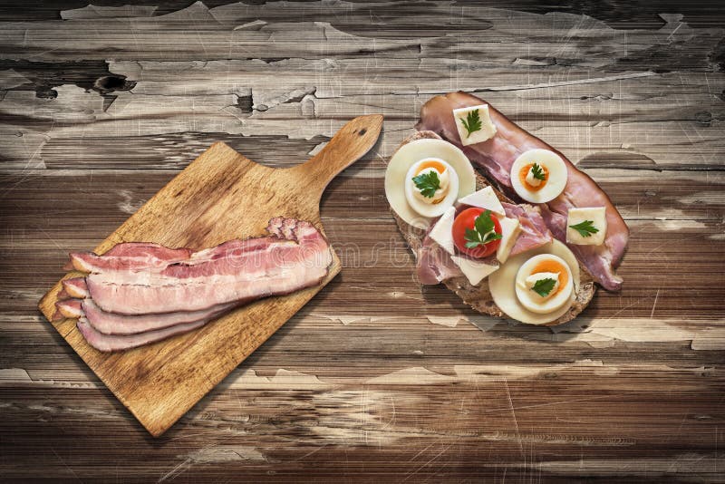 Ham And Cheese and Cherry Tomato Sandwich with Bacon Rashers on Cutting Board, set on Old Wooden Garden Table Surface