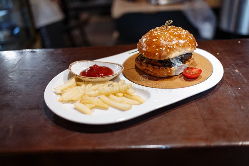Hamburgare dekorerad tomat, franska småfiskar och tomatsås i en oval platta på en trätabell fotografering för bildbyråer Hamburgare dekorerad tomat, franska småfiskar och tomatsås i en oval platta på en trätabell fotografering för bildbyråer