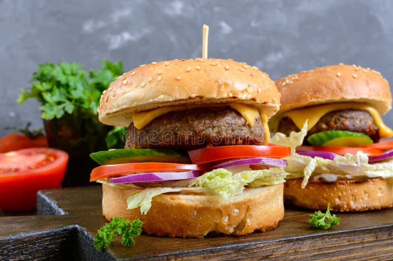 Hamburgare med den saftiga kotletten, nya grönsaker, frasig bulle med sesamfrö på en trätabell Närbild royaltyfria bilder Hamburgare med den saftiga kotletten, nya grönsaker, frasig bulle med sesamfrö på en trätabell Närbild royaltyfria bilder