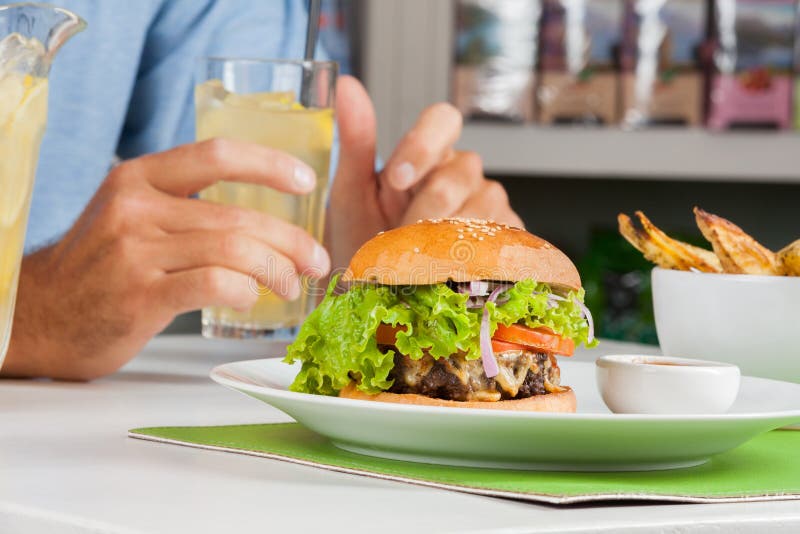 Hamburgare med mans drinken för handinnehav på tabellen arkivfoton Hamburgare med mans drinken för handinnehav på tabellen arkivfoton