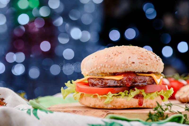 Hamburger avec la côtelette juteuse, les tomates, le fromage, la laitue et la sauce rouge sur le conseil en bois contre la guirla photographie stock libre de droits Hamburger avec la côtelette juteuse, les tomates, le fromage, la laitue et la sauce rouge sur le conseil en bois contre la guirla photographie stock libre de droits