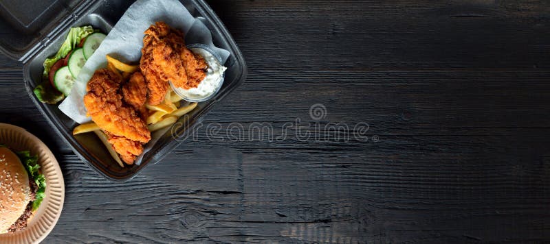 Hamburger, french fries and fried chicken in takeaway containers on the wooden background. Food delivery and fast food concept.