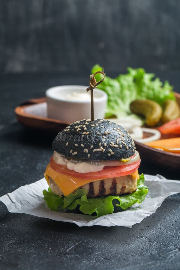 Hamburger nero con il tortino del pollo. Hamburger nero casalingo con il tortino arrostito del pollo su fondo scuro
