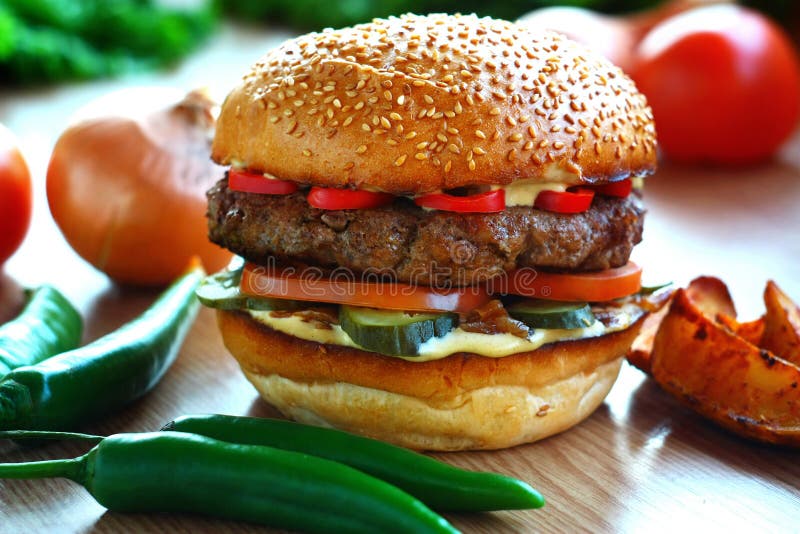 Hamburger succoso e piccante con manzo e peperone, su una tavola con le verdure fotografie stock libere da diritti Hamburger succoso e piccante con manzo e peperone, su una tavola con le verdure fotografie stock libere da diritti