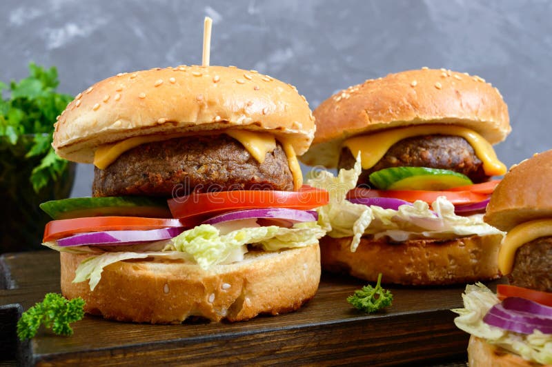 Hamburgers avec la côtelette juteuse, légumes frais, petit pain croustillant avec les graines de sésame sur une table en bois Pla photos stock Hamburgers avec la côtelette juteuse, légumes frais, petit pain croustillant avec les graines de sésame sur une table en bois Pla photos stock