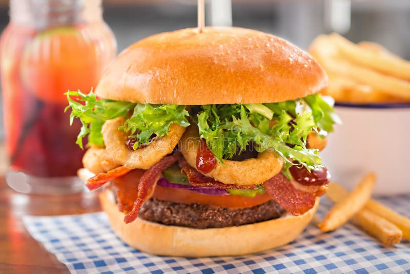 Hamburguesa con carne de vaca, el tomate, la cebolla, las salmueras, el tocino, los anillos de cebolla, la lechuga y la salsa de fotografía de archivo Hamburguesa con carne de vaca, el tomate, la cebolla, las salmueras, el tocino, los anillos de cebolla, la lechuga y la salsa de fotografía de archivo