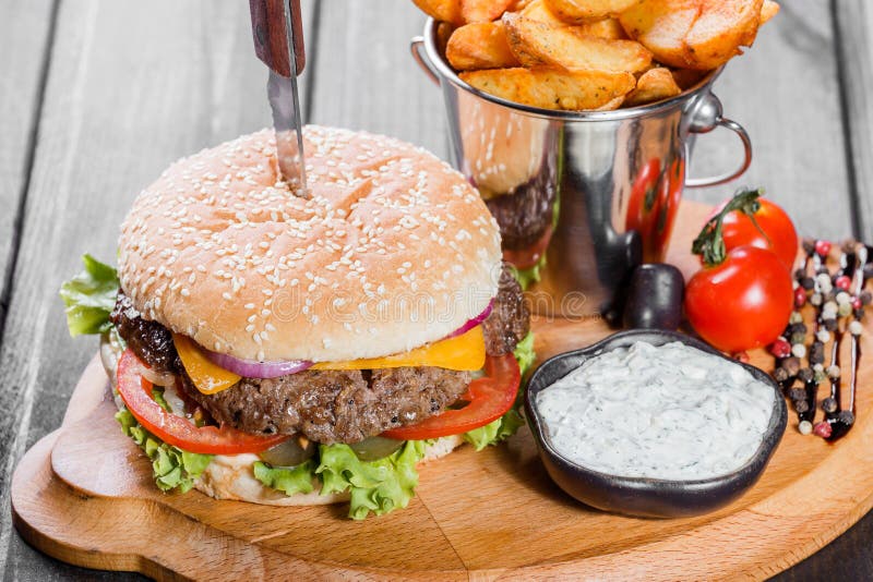 Hamburguesa con las verduras frescas, el queso, la salsa y las fritadas en tabla de cortar fotografía de archivo libre de regalías Hamburguesa con las verduras frescas, el queso, la salsa y las fritadas en tabla de cortar fotografía de archivo libre de regalías