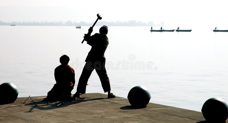 Silhouette of a workman swinging a large sledgehammer while repairing a concrete, waterfront dock. Silhouette of a workman swinging a large sledgehammer while repairing a concrete, waterfront dock.