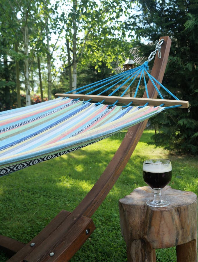 A colorful garden hammock rests in the shade with a cold beverage nearby. A colorful garden hammock rests in the shade with a cold beverage nearby