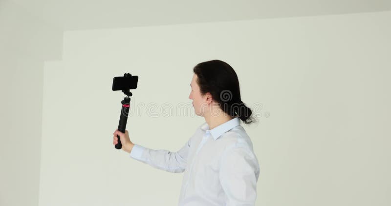Han har en smartphone på stabilisatorn och tar sig självt på vit bakgrund arkivfilmer