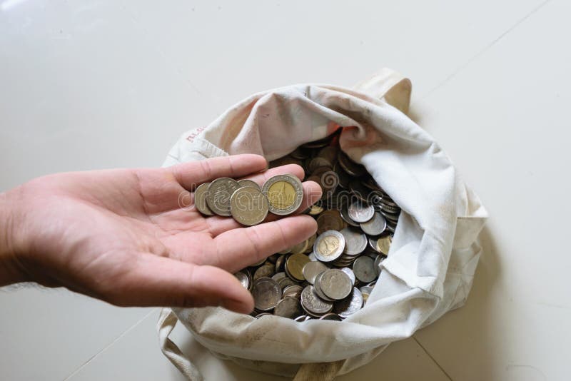 The hands are picked up silver coins into the old bag white,with white background ,image focus on a coin cells. The hands are picked up silver coins into the old bag white,with white background ,image focus on a coin cells