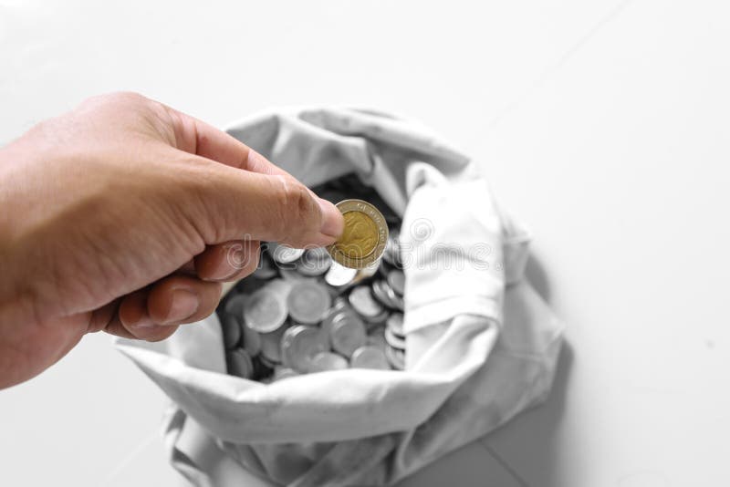 The hands are picked up silver coins into the old bag white,with white background ,image focus on a coin cells. The hands are picked up silver coins into the old bag white,with white background ,image focus on a coin cells