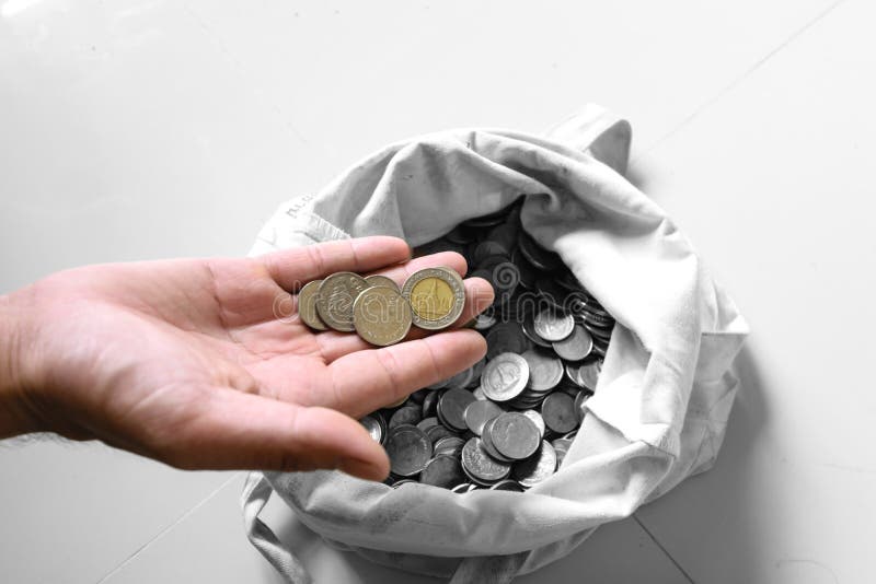 The hands are picked up silver coins into the old bag white,with white background ,image focus on a coin cells. The hands are picked up silver coins into the old bag white,with white background ,image focus on a coin cells