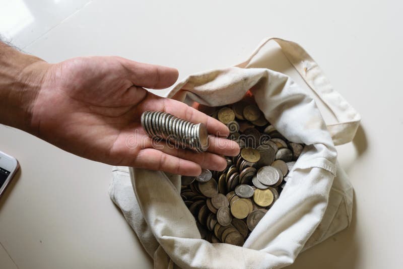 The hands are picked up silver coins into the old bag white,with white background ,image focus on a coin cells. The hands are picked up silver coins into the old bag white,with white background ,image focus on a coin cells