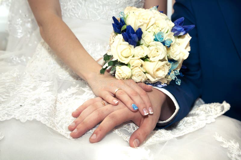 Hand av brudgummen i handen av bruden med den härliga brud- buketten i händer royaltyfri foto Hand av brudgummen i handen av bruden med den härliga brud- buketten i händer royaltyfri foto