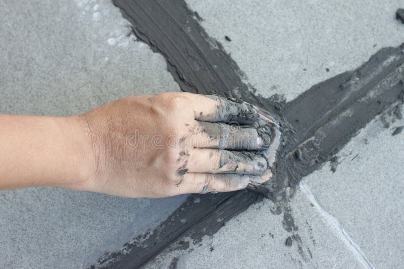 Hand av teknikerbruk av den rubber durken på grå färg av den nya grouttegelplattan arkivbild Hand av teknikerbruk av den rubber durken på grå färg av den nya grouttegelplattan arkivbild