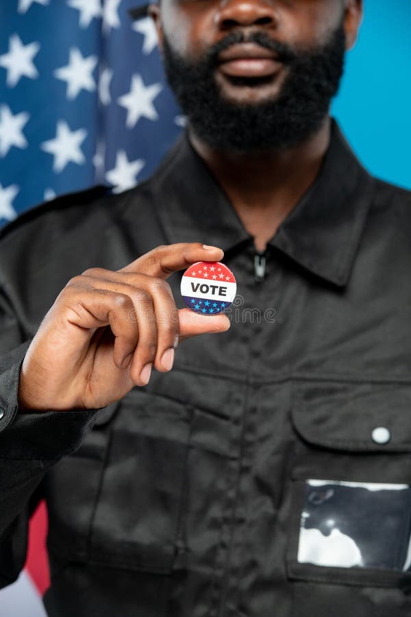 Hand of bearded African male security in black uniform showing you vote insignia. Hand of bearded African-american male security in black uniform showing you stock photos Hand of bearded African male security in black uniform showing you vote insignia. Hand of bearded African-american male security in black uniform showing you stock photos