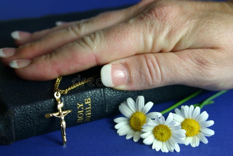 Hand resting on bible with gold crucifix and flowers. Hand resting on bible with gold crucifix and flowers