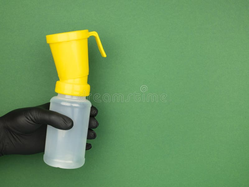 Hand in black nitrile glove holds a teat dip cup for udder cow disinfection on the green background, copy space
