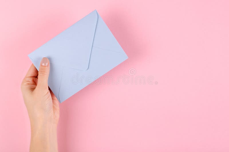 Hand with blue paper envelope composition on pink background