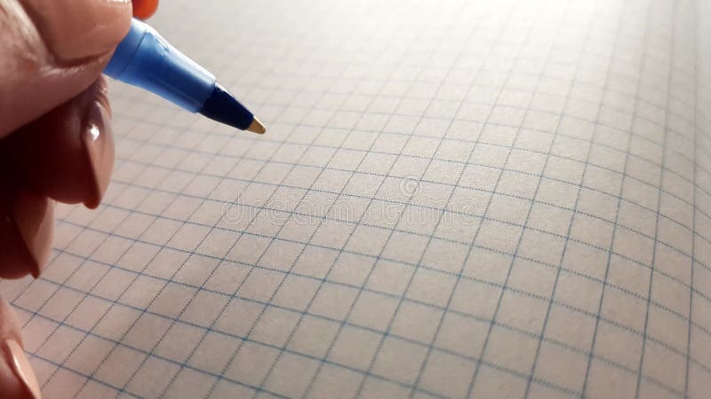 Hand with a blue pen over a squared notebook.