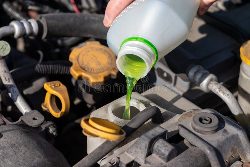 Hand with bottle pouring antifreeze coolant into the expansion tank. Dusty details of a flat-four boxer car engine compartment