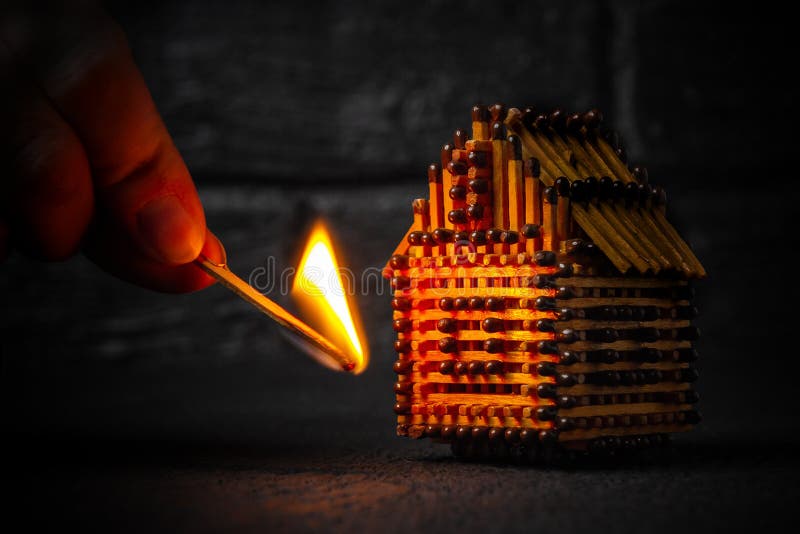 Hand with a burning match sets fire to the house model of matches, risk, property Insurance protection or ignition of combustible