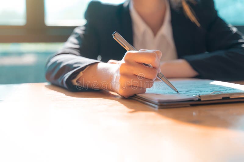 Hand of businesswoman sitting at the table and writing on business contract in office stock image Hand of businesswoman sitting at the table and writing on business contract in office stock image