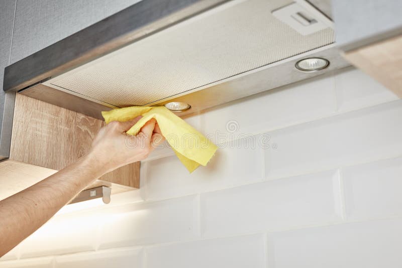 Hand cleaning kitchen hood with yellow washcloth closeup