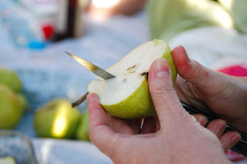 Hand cutting a pear with knife during picnic