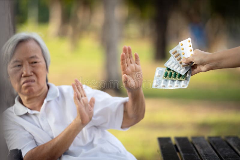 Hand der Bezugsperson -kapseln Medizinpillen und geben der alten asiatischen älteren Frau, die sich weigert, Arzneimittel Angst sc