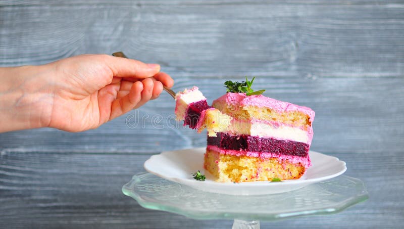 Hand die een vork met een plak van cake houden die, van een stuk die van cake wordt gespleten, uit roze, wit, zand en robijnrode