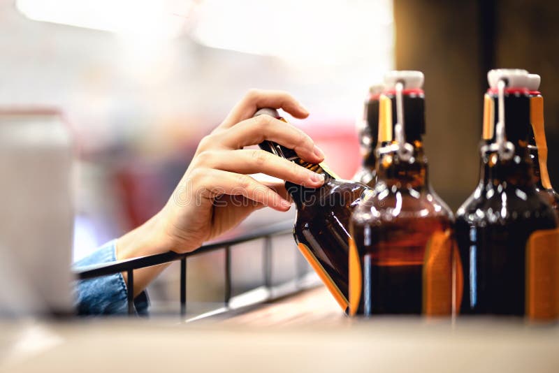 Hand taking bottle of beer from shelf in alcohol and liquor store. Customer buying cider or supermarket staff filling and stocking shelves. Retail worker working. Woman choosing lager or pale ale. Hand taking bottle of beer from shelf in alcohol and liquor store. Customer buying cider or supermarket staff filling and stocking shelves. Retail worker working. Woman choosing lager or pale ale