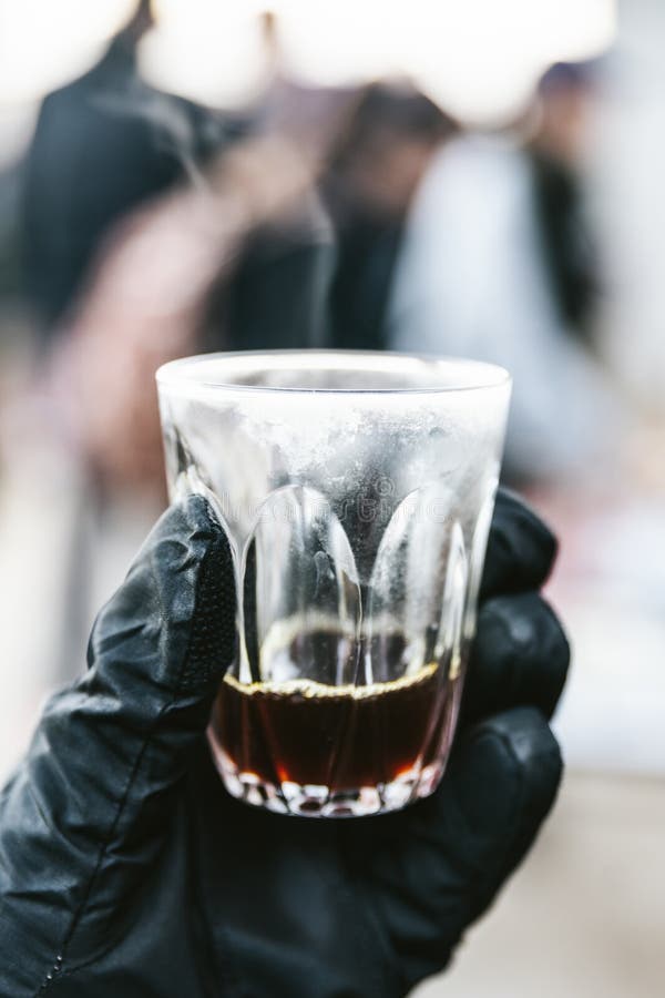 Hand die handschoen dragen die een schot van druipende espresso in het drinken van glas met stoom en onduidelijk beeldachtergrond stock afbeeldingen Hand die handschoen dragen die een schot van druipende espresso in het drinken van glas met stoom en onduidelijk beeldachtergrond stock afbeeldingen