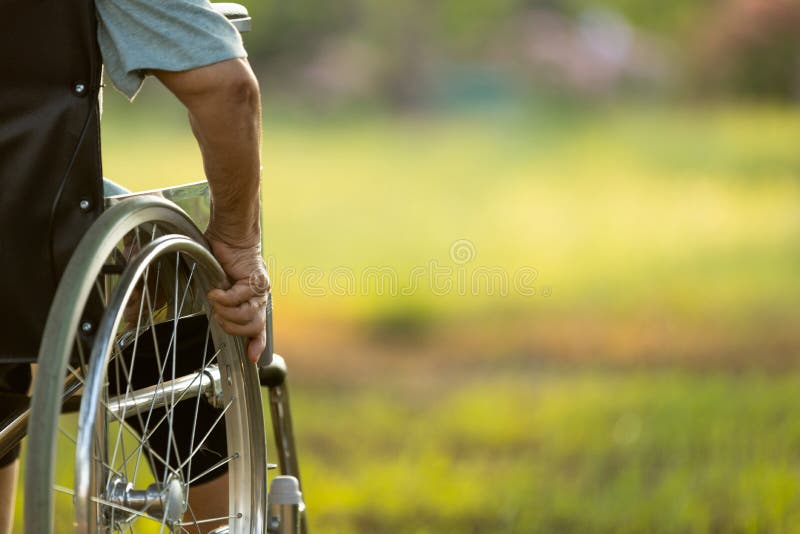 Hand of disabled elderly person outside in green nature at park,copy space,old woman sitting on her wheelchair looking forward