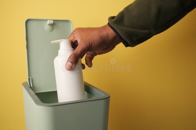 Hand disposing of a white bottle in a green trash can royalty free stock photography