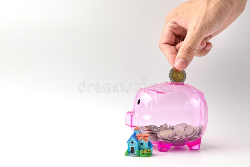 Hand drop coins on clear pink piggy bank and house model on whit