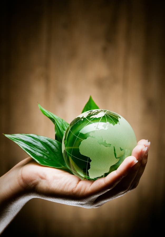 La mano dell'uomo con l'eco di vetro verde globo del pianeta Terra con le foglie fresche, sfondo marrone.