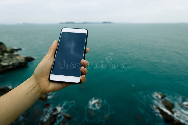 Hand genom att använda smartphonen med havet royaltyfri fotografi Hand genom att använda smartphonen med havet royaltyfri fotografi