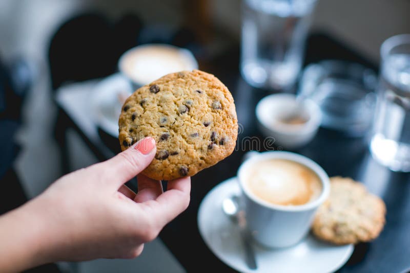 hand holding a cookie with cups of coffee in the background