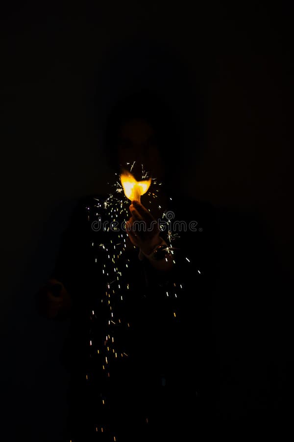 Hand Holding a Flame in the Dark. Magic Trick. Sparks of Fire on Black